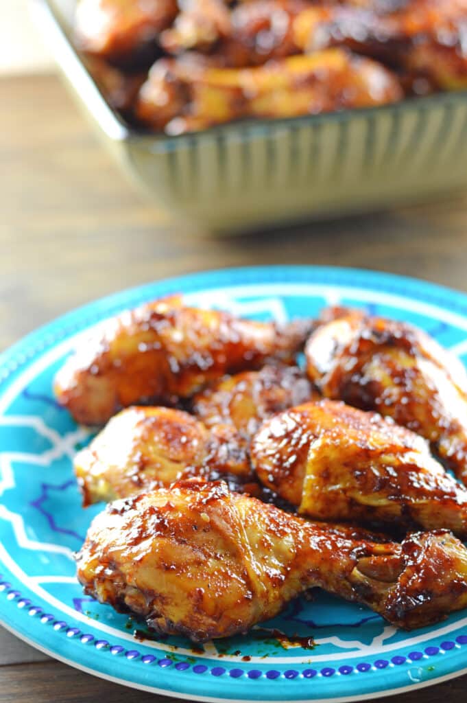 BBQ drumsticks on a light blue plate with another big grey bowl in the back full of drumsticks