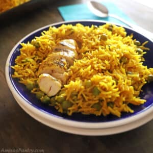 Yellow rice and chicken place on a dark blur plate with white rim