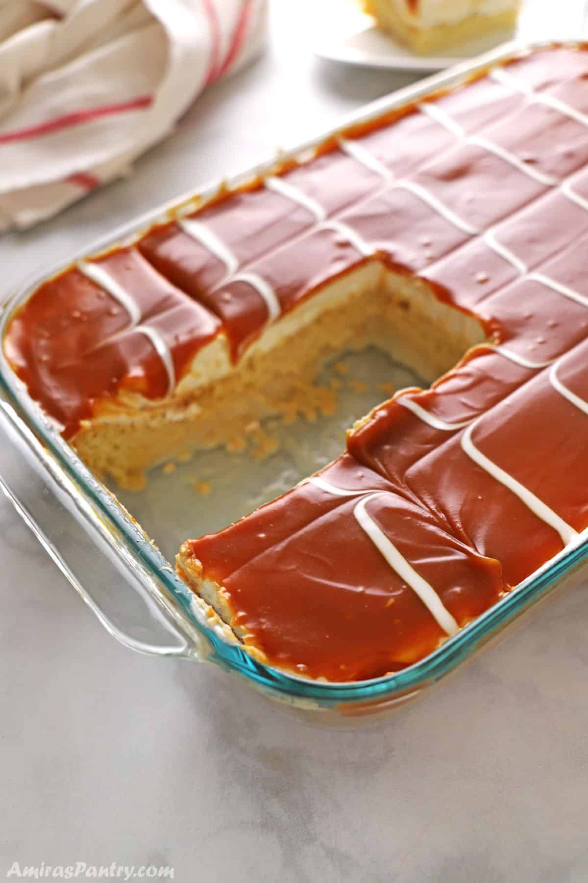 A casserole of tres leches placed on a white marble table with a couple of pieces taken out.