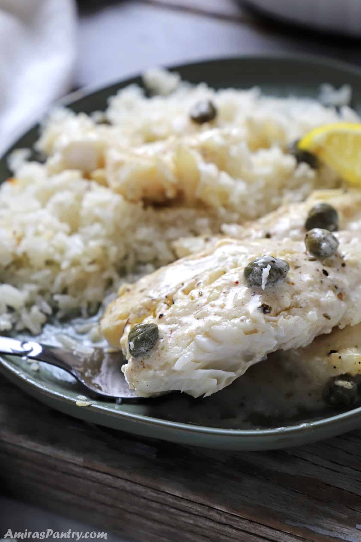 A green plate with white rice and baked cod.