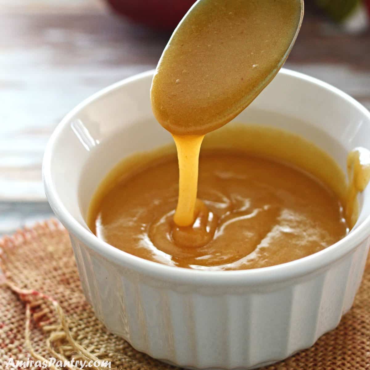 A spoon pouring some date caramel into a white bowl.