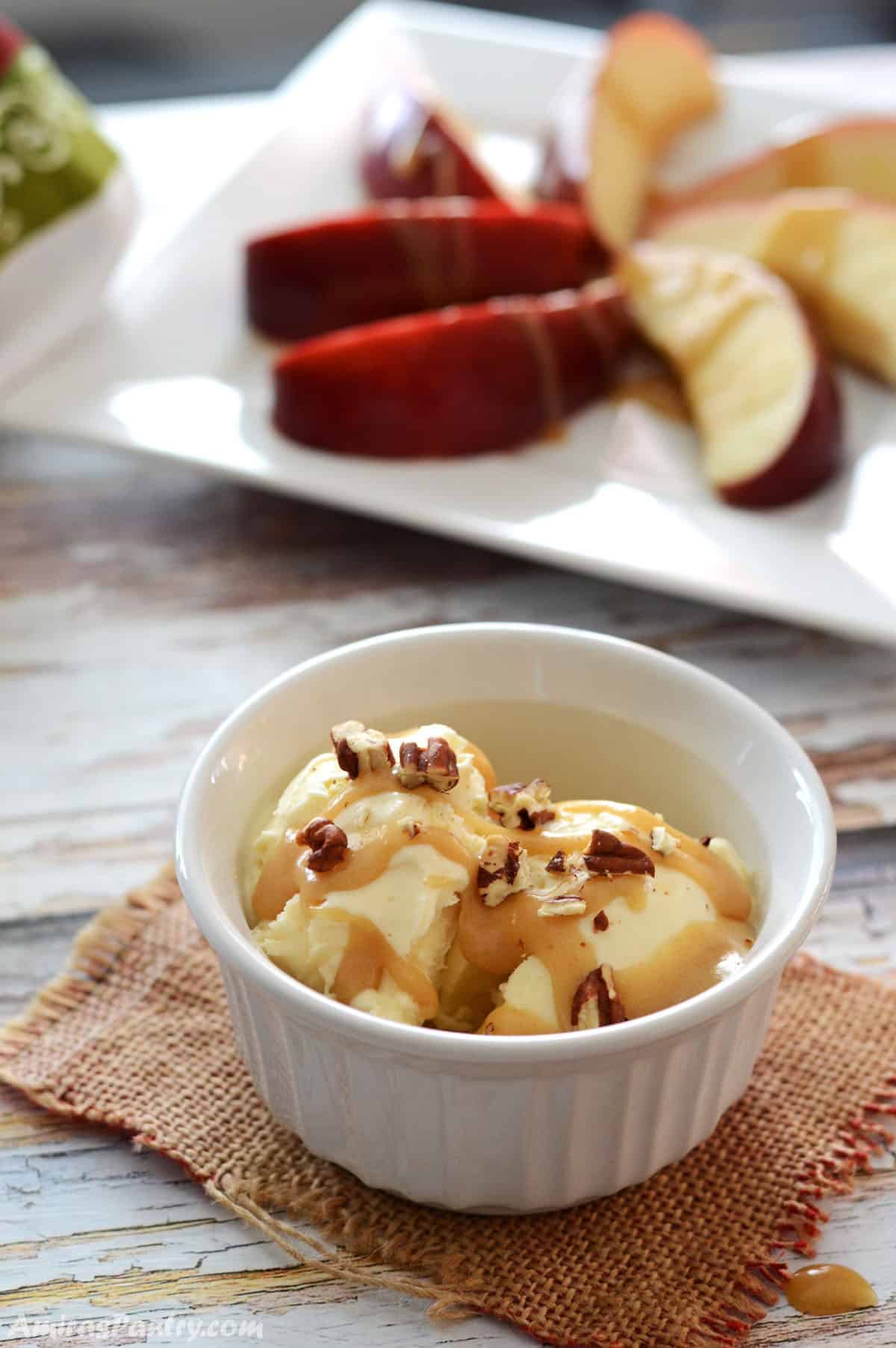 A small white ramekin with ice cream drizzled with date caramel and pecan pieces.