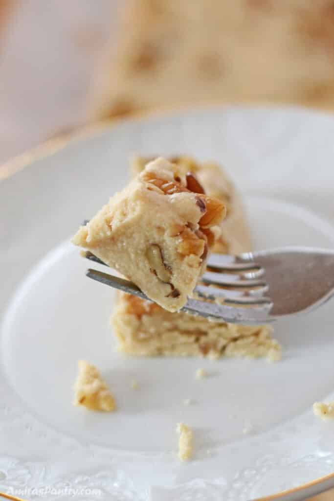 A fork holding a piece of halva with the rest on a white plate.