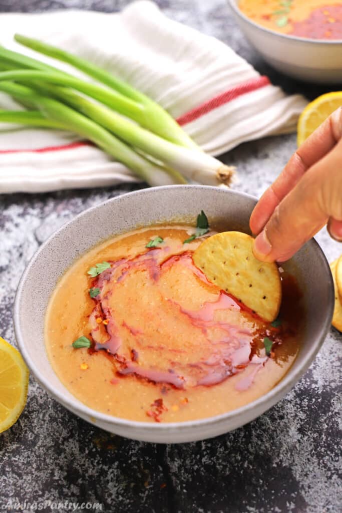 A hand dipping a cracker in the soup bowl.