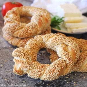 Turkish simit placed on a concrete surface with a plate of white cheese on the back