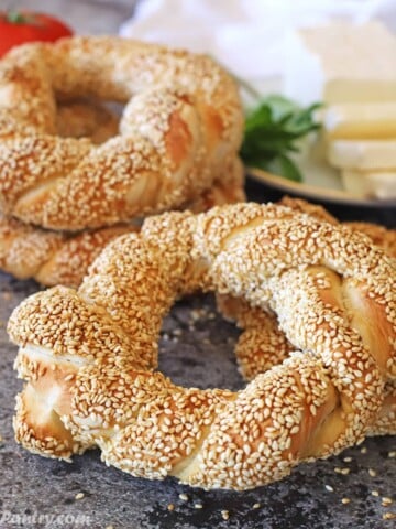 Turkish simit placed on a concrete surface with a plate of white cheese on the back