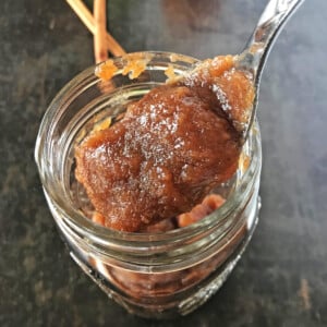 A jar filled to the brin with apple butter with a spoon scooping some out of the jar.