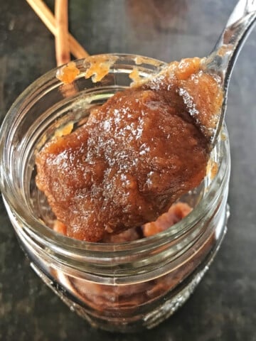 A jar filled to the brin with apple butter with a spoon scooping some out of the jar.