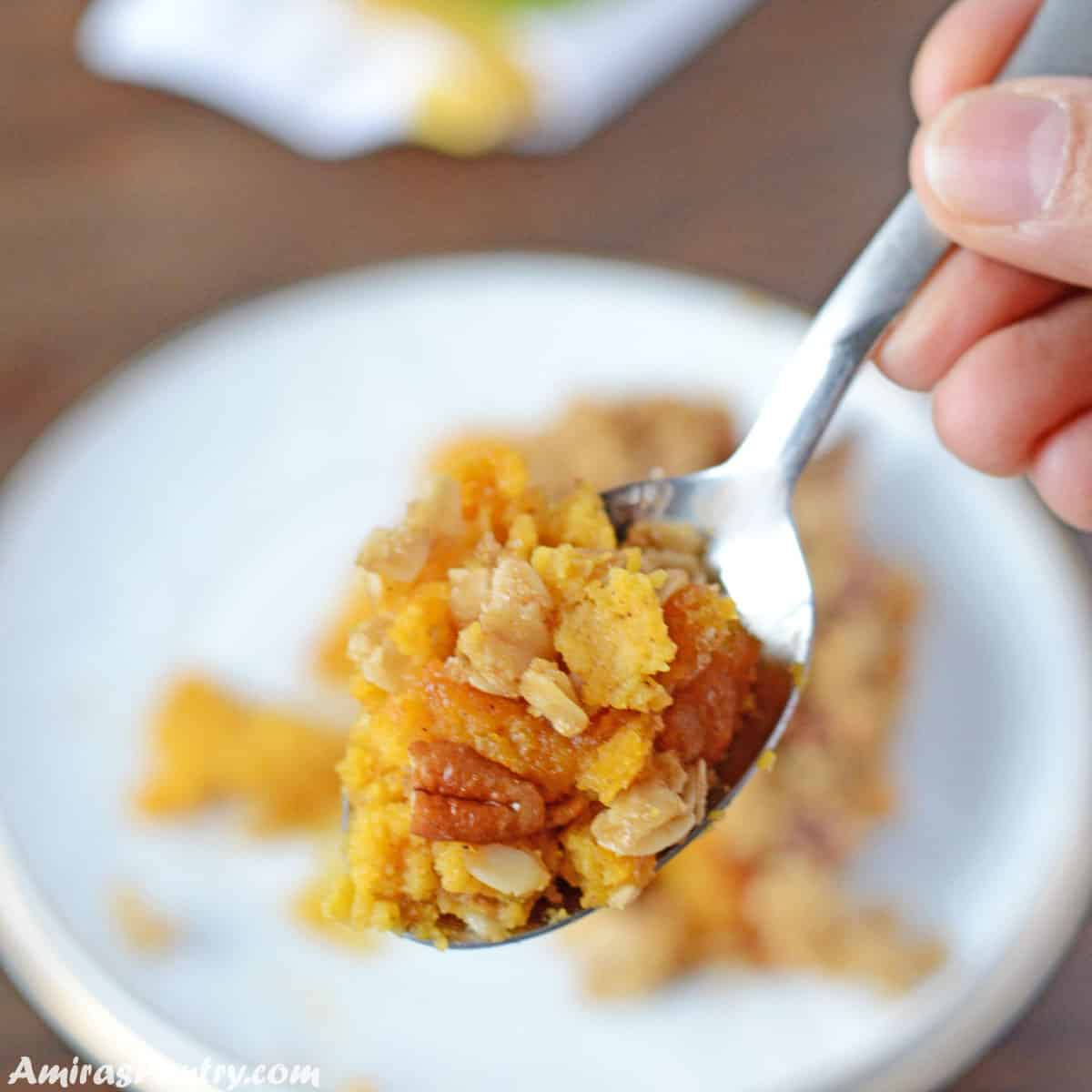 A hand holding a spoon scooping some butternut squash with the crunchy topping.