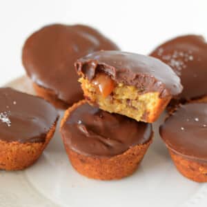 Chocolate caramel cups on top of each other on a white plate with a bite take from one showing some caramel dripping.