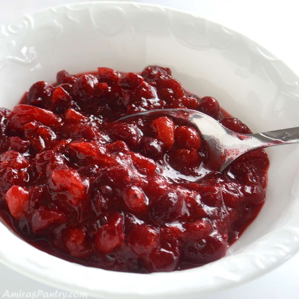Cranberry sauce in a white bowl with a spoon in it.