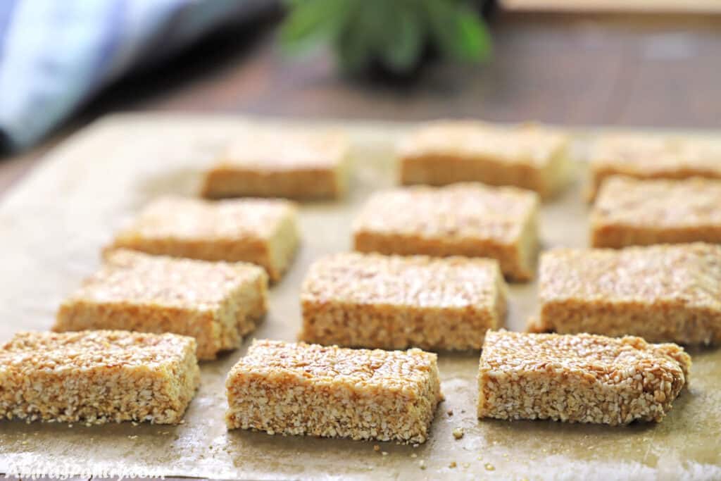 Sesame bars on a parchment paper placed on a wooden board.