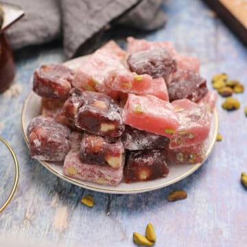 Pink and red Turkish delight squares on a white plate placed on a wooden countertop.
