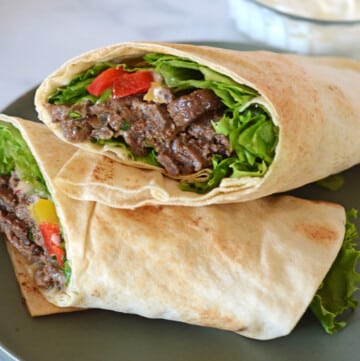 two halves of a beef shawarma wraps stacked on a green plate.