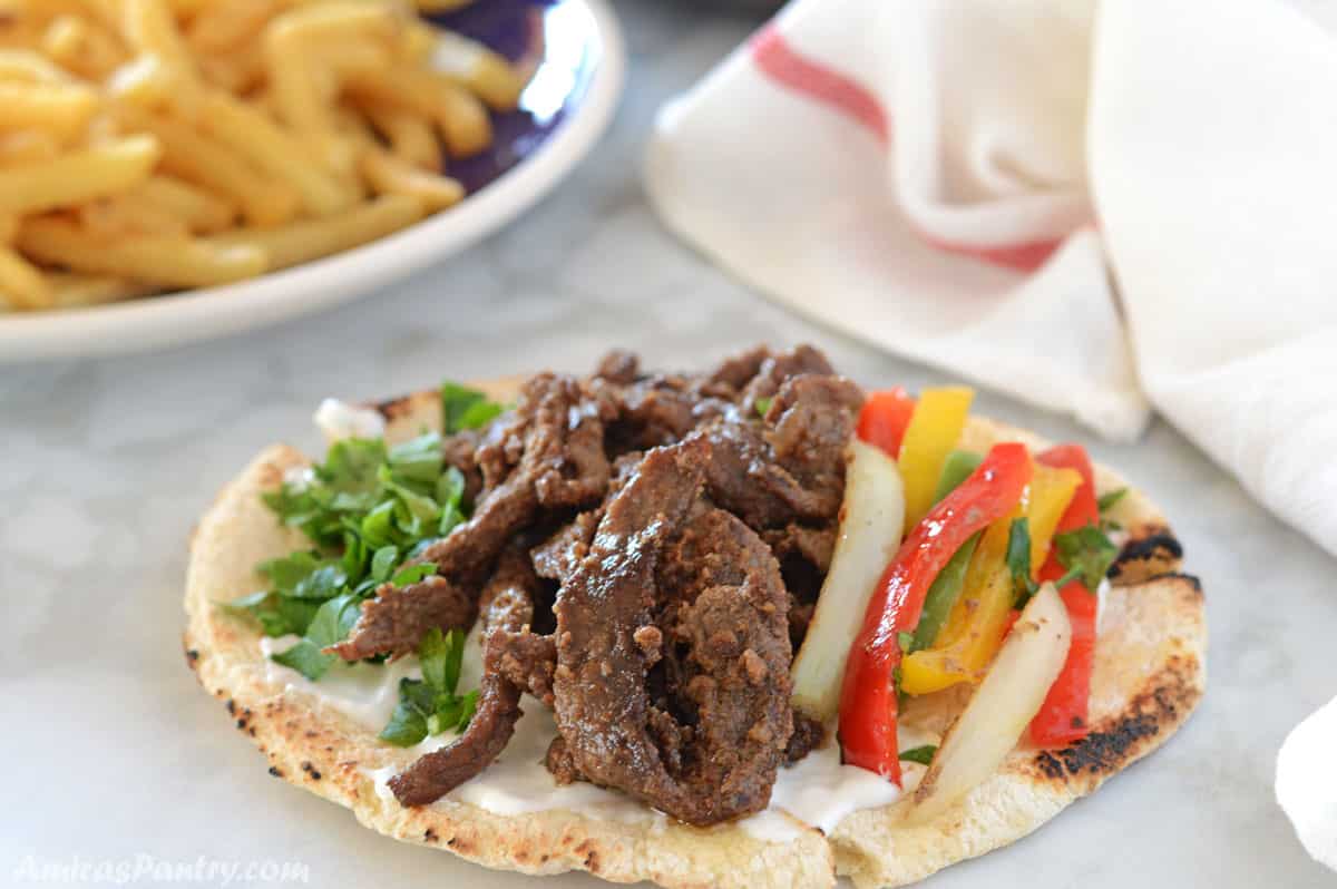Beef shawarma strips on a pita bread with lettuce, parsley and onions.