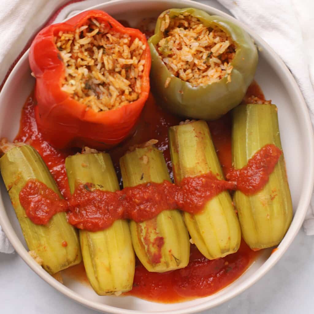 A serving plate with stuffed zucchini and bell peppers with tomato sauce.