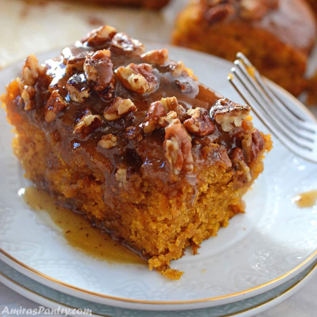 A piece of pecan pumpkin cake on a white dessert plate with a fork next to it.