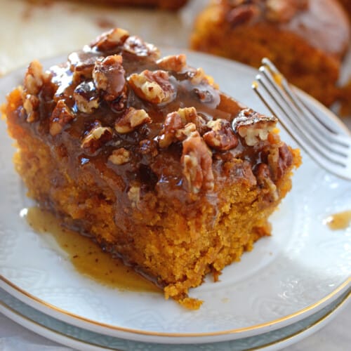 A piece of pecan pumpkin cake on a white dessert plate with a fork next to it.