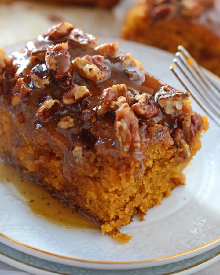 A piece of pecan pumpkin cake on a white dessert plate with a fork next to it.