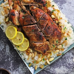 A whole duck placed on a serving platter over a bed or rice garnished with roasted nuts.