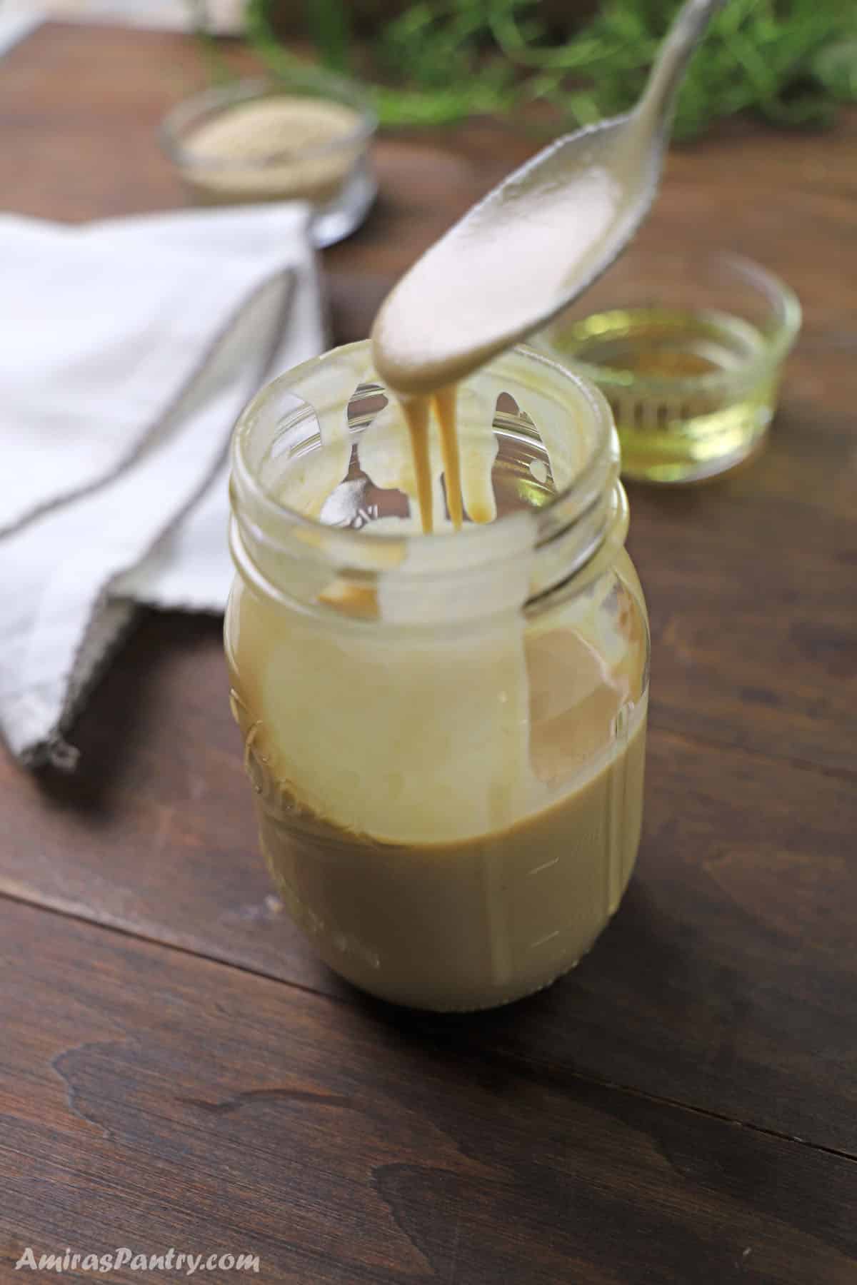 A spoon pouring some homemade tahini in a jar.