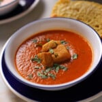 A bowl of tomato basil soup with some croutons on the top.