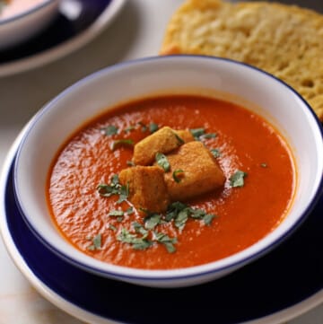 A bowl of tomato basil soup with some croutons on the top.