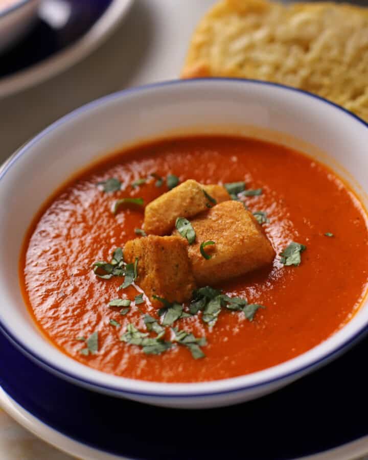 A bowl of tomato basil soup with some croutons on the top.