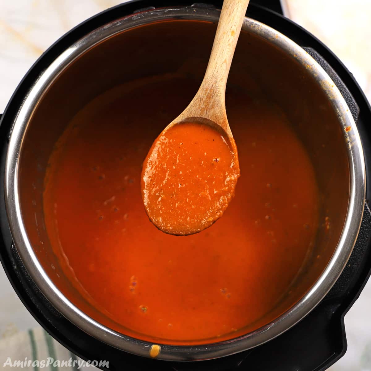 A wooden spoon scooping some tomato soup out of the instant pot.