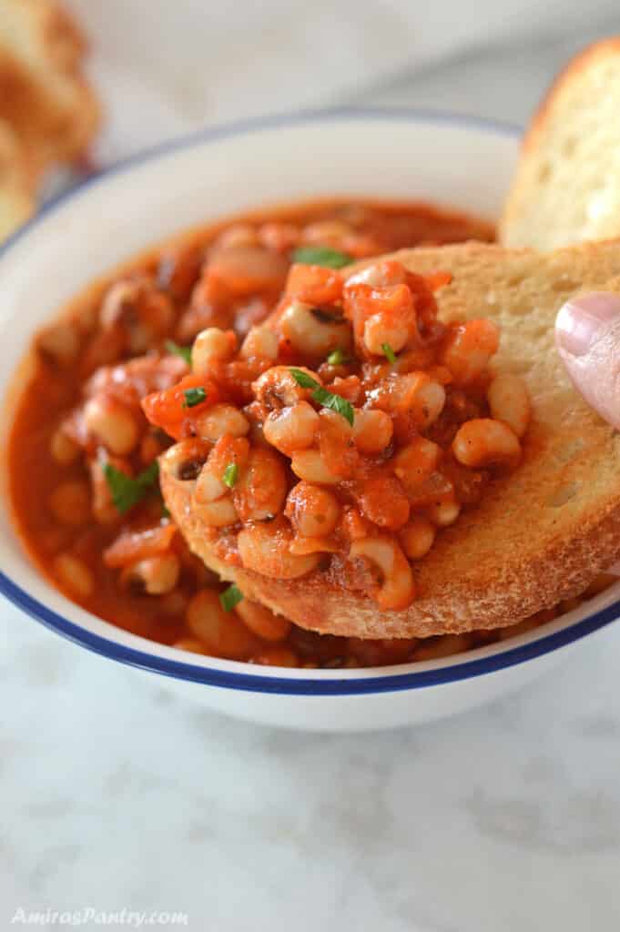 A hand holding a piece of bread scooping some black peas stew.