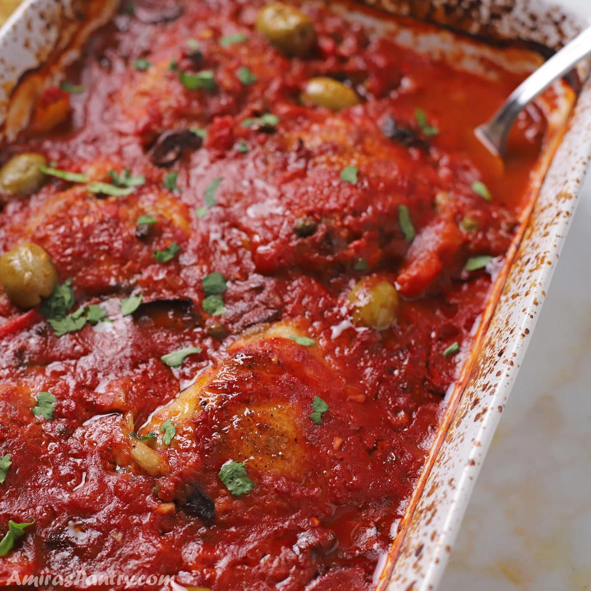 A white oven dish with chicken cacciatore and a spoon in it.