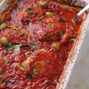 A white oven dish with chicken cacciatore and a spoon in it.