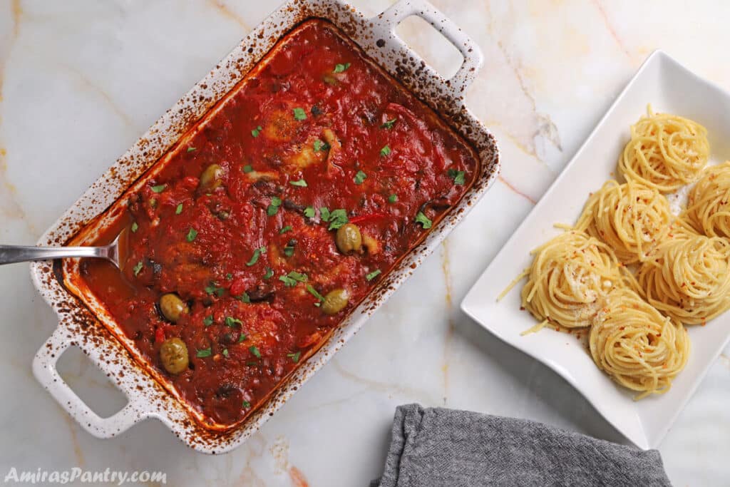 Chicken Cacciatore in a white baking dish with another serving dish of pasta next to it.
