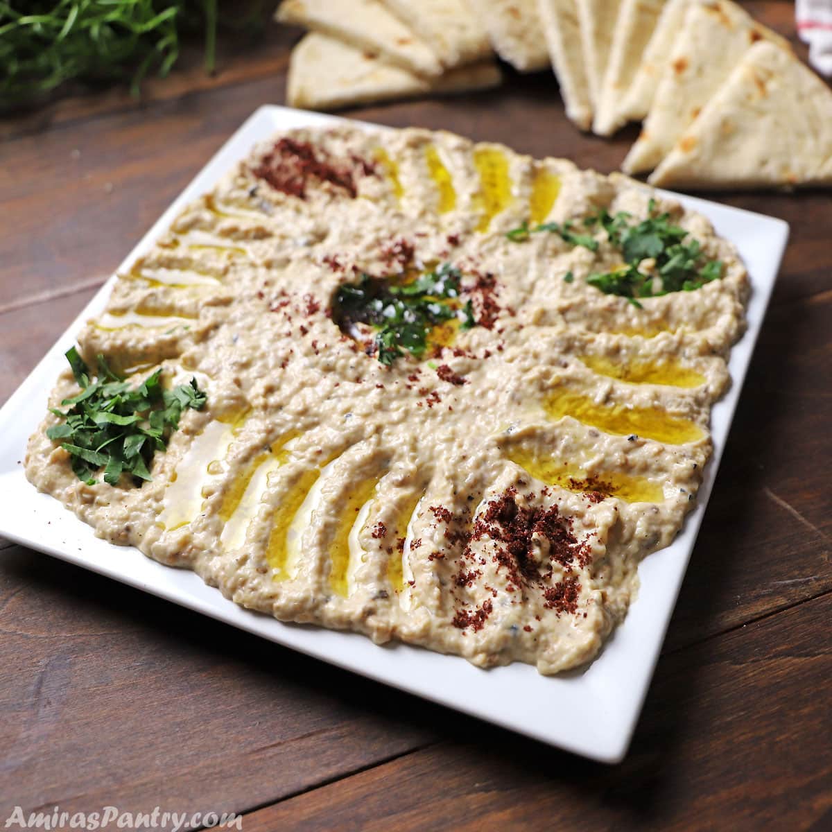 Mutabal dip in a white square plate garnished with sumac and chopped parsley.