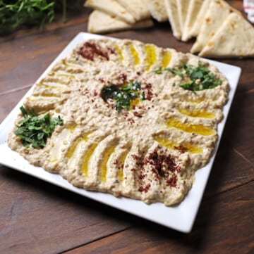 Mutabal dip in a white square plate garnished with sumac and chopped parsley.