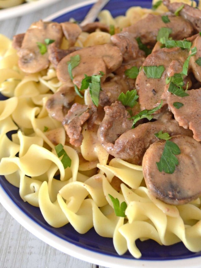 Beef stroganoff served over pasta on a blue plate with white rim.