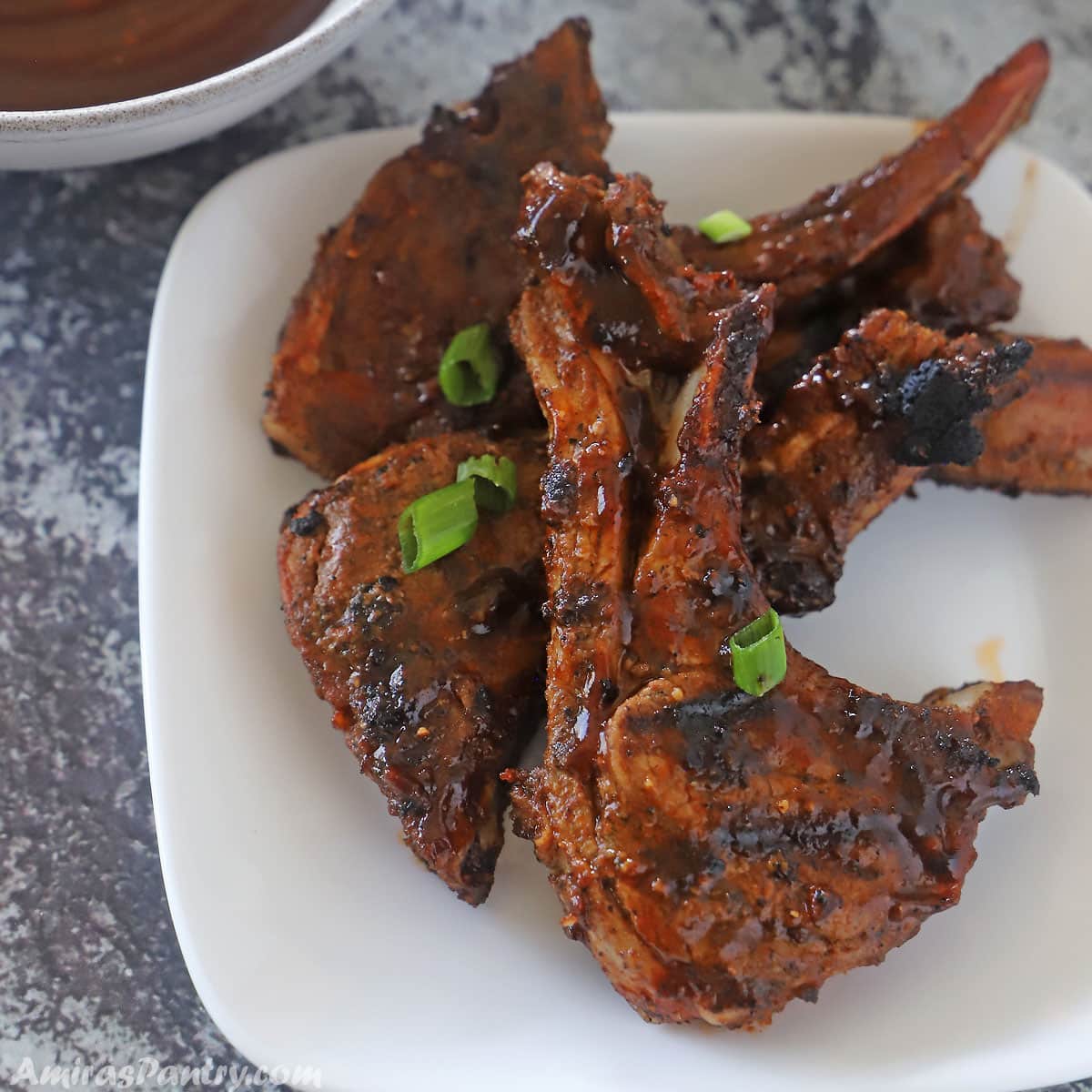 Lamb chops on a white serving plate garnished with chopped spring onions.