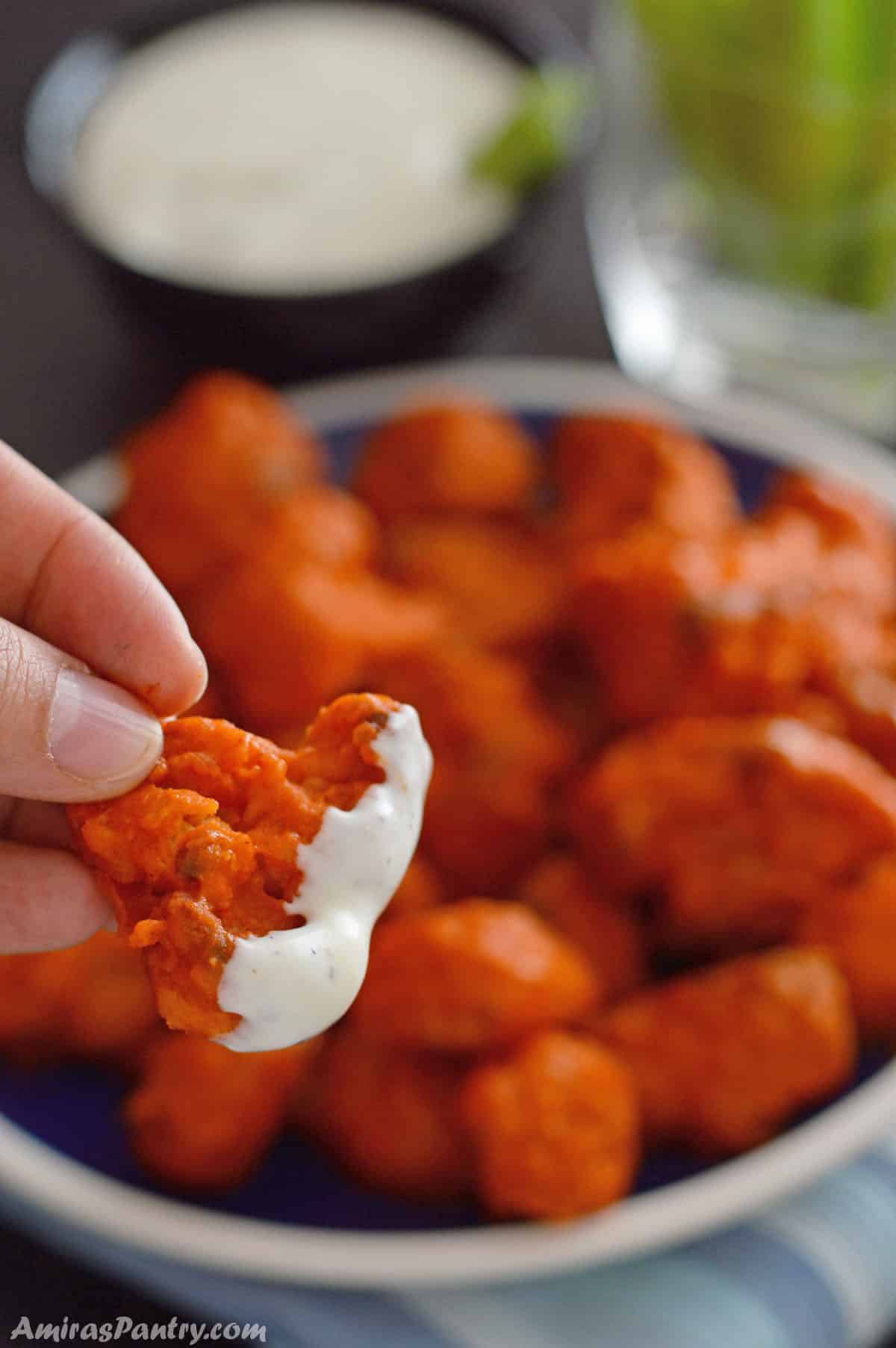 A hand holding a piece of crispy buffalo cauliflower dipped in ranch sauce.