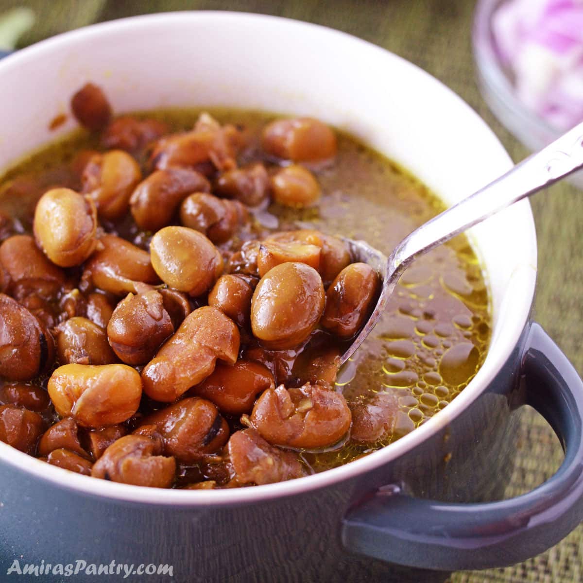 A bowl of ful with a spoon scooping some of the beans out.