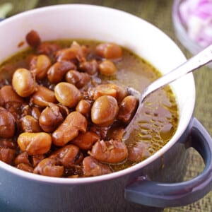 A bowl of ful with a spoon scooping some of the beans out.
