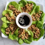 A serving platter filled with chicken lettuce wraps and a sauce bowl in the middle.