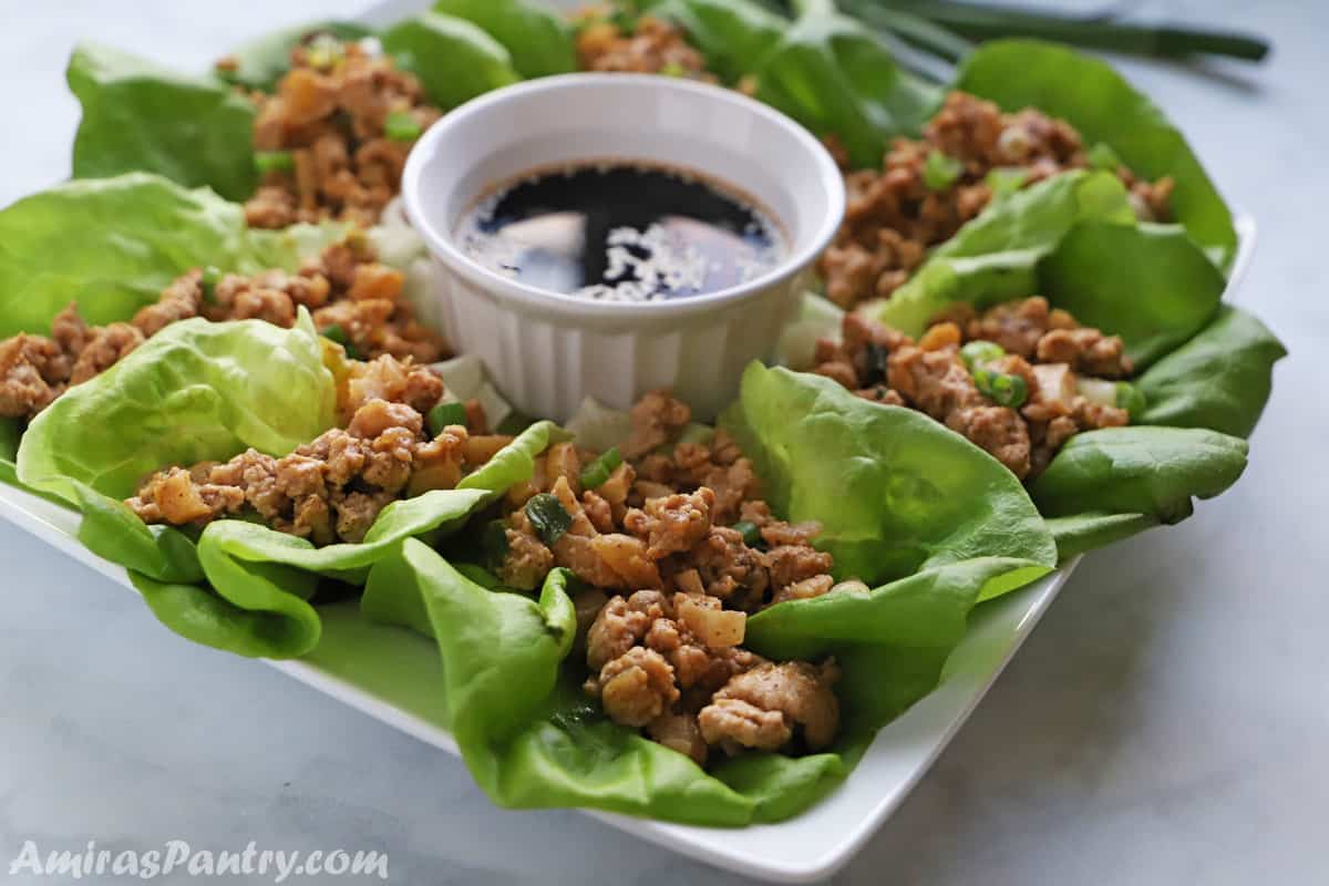 chicken lettuce wraps in a white platter with a bowl of sauce.