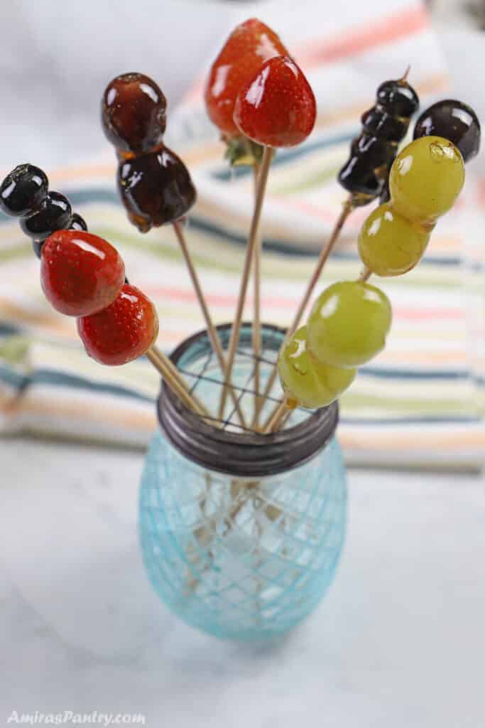 Tanghulu skewers on a blue vase and placed on a white marble surface.