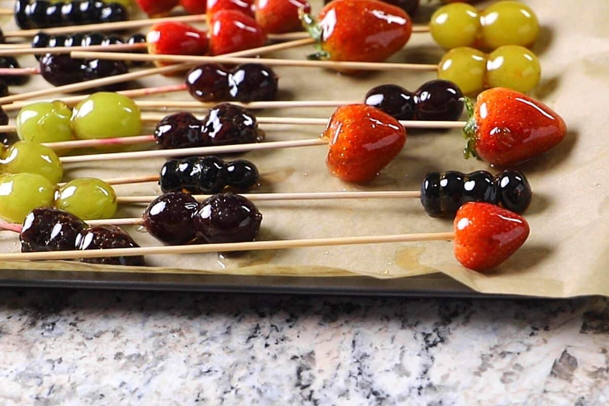 Tanghulu candied fruits on skewers and placed on a baking sheet lined with parchment paper.