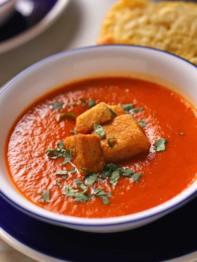 Tomato soup in a white bowl with a blue rim garnished with chopped basil.