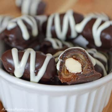 Chocolate covered dates in a white bowl with one cut open to show texture.