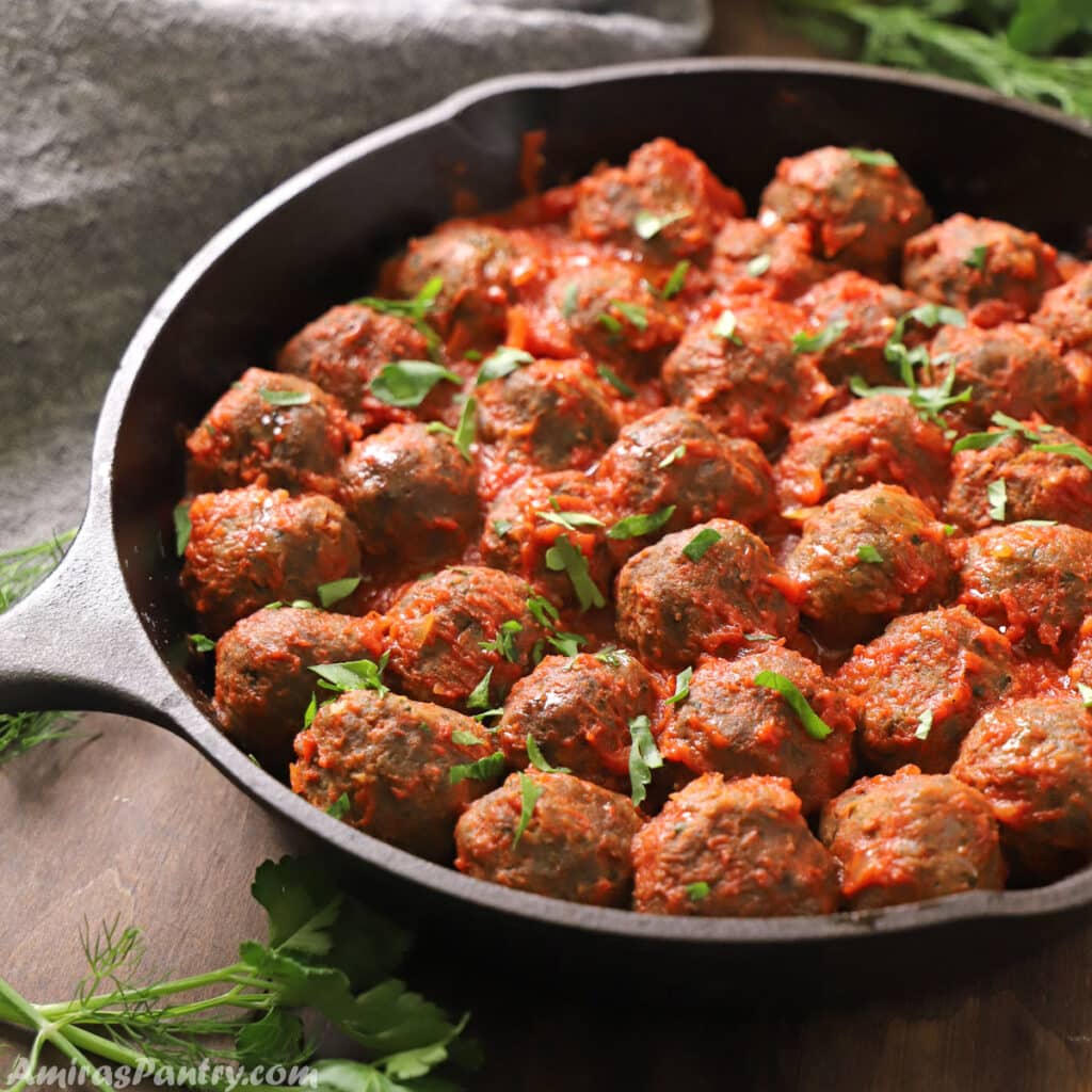 Meatballs in a cast iron skillet with tomato sauce and garnished with parsley.