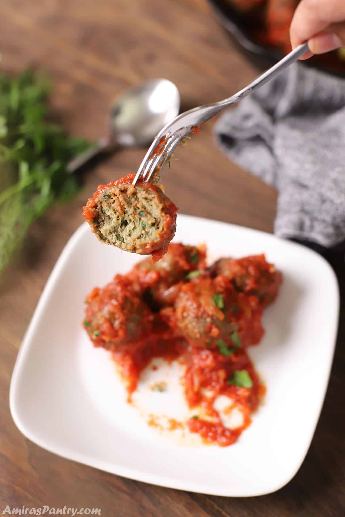 A hand holding a fork with a gluten free meatball cut to show texture.