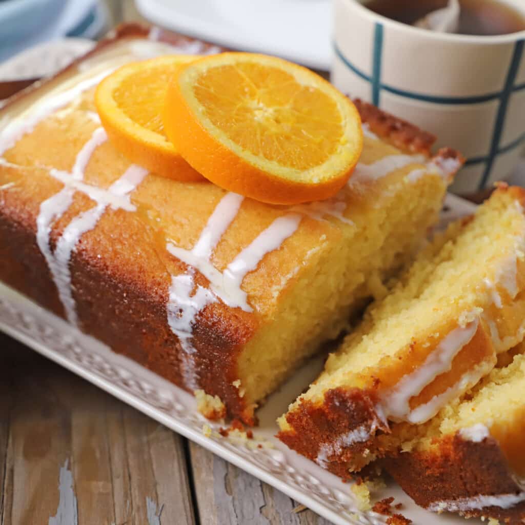 An orange cake slices and placed on a white platter with orange slices on top.