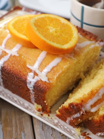 An orange cake slices and placed on a white platter with orange slices on top.